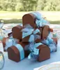 A stack of brown gift boxes tied with light blue ribbon and tulle, arranged on a light blue tablecloth outdoors. Náhled obrázku produktu