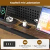 A close-up view of a bed frame's headboard with integrated charging features, showing a phone, smartwatch, and tablet connected to charging ports. Produktbild-Vorschau