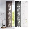 Three different colored panel curtains with a leaf pattern are displayed side-by-side in front of a window. A decorative branch in a vase is placed to the left of the leftmost curtain. Produktbild-Vorschau