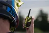 A person wearing a helmet holds a yellow and black walkie-talkie. Náhled obrázku produktu