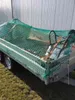 A green net covers a trailer loaded with items, parked outdoors on grass. Produktbild-Vorschau