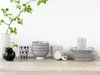 A collection of ceramic tableware, including bowls, mugs, and plates, arranged on a wooden shelf against a white background. Produktbild-Vorschau