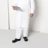 A person wearing a white lab coat and white pants, standing and holding a clipboard, wearing black shoes. Produktbild-Vorschau
