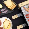 A raclette grill with food items like cheese, shrimp, and vegetables arranged around it. Produktbild-Vorschau