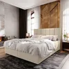 A bedroom scene featuring a large bed with a beige upholstered headboard and base, dressed in white bedding. The room has a modern, minimalist aesthetic with textured walls and wooden accents.