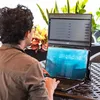 A person is using a dual-screen laptop setup outdoors. Voir les images du produit