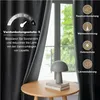 A dark gray curtain is partially drawn, revealing a window with greenery outside. A small lamp sits on a wooden table in front of the window. Text and icons describe the curtain's features. Voir les images du produit