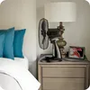 A bedside table with a fan, lamp, and framed picture. Anteprima dell’immagine prodotto