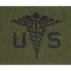 A black medical caduceus symbol with the letters 'US' on either side, set against a green, textured background that resembles grass or felt. Produktbild-Vorschau