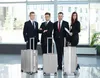 Four business professionals stand in a modern lobby with their luggage. Produktbild-Vorschau