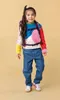 A young girl wearing a colorful sweater and jeans, with a backpack on. Produktbild-Vorschau