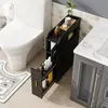A bathroom scene with a toilet, a narrow black storage cabinet with a drawer pulled out, and a vanity cabinet. Produktbild-Vorschau