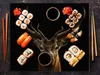 A surreal arrangement of sushi and a deer's head on a black surface, with chopsticks and soy sauce. Produktbild-Vorschau