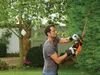 A man is using a hedge trimmer to trim a large green hedge in a garden setting. Anteprima dell’immagine prodotto
