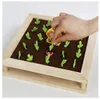 A hand is placing a green felt carrot into a wooden garden board game. Voir les images du produit