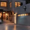 A modern house exterior at dusk, featuring a garage, entrance, and outdoor lighting. Produktbild-Vorschau