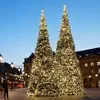 Two large, illuminated Christmas trees on a city street at dusk, with buildings and streetlights in the background. Voir les images du produit