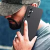 A person wearing a cap and t-shirt is holding a black smartphone case to their ear. Produktbild-Vorschau