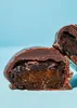 A close-up shot of a chocolate-covered plum, cut in half, against a light blue background. Produktbild-Vorschau