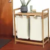 A bamboo laundry basket with two beige fabric bags, placed in a room with a wooden door and floor. Anteprima dell’immagine prodotto
