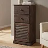 A dark brown wooden cabinet with two drawers and a louvered door, placed on a wooden floor next to a cream-colored armchair. Podgląd zdjęcia produktu
