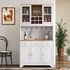 A white buffet with glass doors and wooden accents, styled with wine bottles, glasses, and decorative jars, in a room with a chair and a plant. Produktbild-Vorschau