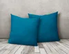Two teal pillows are leaning against a textured gray wall on a wooden floor. Produktbild-Vorschau