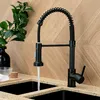 A black kitchen faucet with a pull-down sprayer is shown in use, with water flowing into a sink. The background is a wooden wall. Produktbild-Vorschau