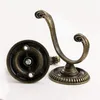 Two bronze-colored vintage-style hooks are shown against a white background. One hook is upright, showing its curved shape and decorative top. The other hook is lying on its side, revealing its circular base and the screw mechanism for attachment. Produktbild-Vorschau