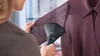 A person is using a handheld garment steamer to remove wrinkles from a purple shirt. Voir les images du produit
