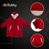 A red hoodie blanket with white trim and a large front pocket, displayed against a black background with geometric gold accents. Insets show close-ups of the material and pocket. Anteprima dell’immagine prodotto