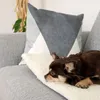 A small brown dog is resting on a white fluffy blanket on a gray sofa, with a decorative pillow in the background. Náhľad obrázku produktu