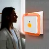 A woman stands in a dimly lit room, looking towards a wall-mounted night light. Produktbild-Vorschau