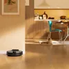 A robot vacuum cleaner is on a wooden floor in a modern home, with a cat lying on a rug in the background. Produktbild-Vorschau