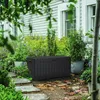 A dark gray storage box sits on a garden path surrounded by plants and foliage. Podgląd zdjęcia produktu