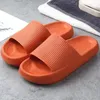 Paar leuchtend orangefarbene Cloud-Slide-Sandalen auf grauem Boden neben einem weiß-grauen Handtuch Náhľad obrázku produktu