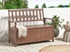 A wooden garden bench with storage is placed on a wooden deck, next to a white wall and some greenery. Náhled obrázku produktu