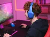 A young person wearing blue gaming headphones is playing a video game on a computer. Voir les images du produit