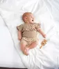 A baby lying on a white blanket with a wooden rattle. Produktbild-Vorschau