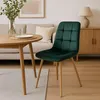 A dark green velvet chair is placed next to a wooden dining table in a well-lit room with a sofa and a cabinet in the background. Anteprima dell’immagine prodotto