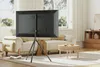 A modern living room with a TV on a tripod stand in the foreground, a sofa and coffee table in the midground, and a window and wooden cabinet in the background. Anteprima dell’immagine prodotto
