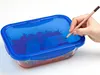 A hand is writing on the lid of a transparent food storage container with a blue lid. Anteprima dell’immagine prodotto