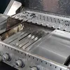 Close-up view of the interior of a gas grill, showing various stainless steel cooking accessories and components. Produktbild-Vorschau