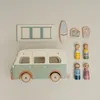 A collection of wooden toys including a vintage camper van, figures, a surfboard, and luggage, arranged on a neutral background. Náhled obrázku produktu