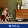 A woman is demonstrating the folding feature of a Tineco Floor One S7 Artist wet dry vacuum cleaner. The vacuum is shown in a folded position, highlighting its compact size. The background includes a dresser with vases of flowers and a green wall. Produktbild-Vorschau