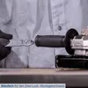A person wearing black gloves is holding a tool near the handle of an angle grinder. Produktbild-Vorschau