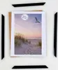 A framed picture of a beach scene with a seagull flying, surrounded by black frame pieces. Produktbild-Vorschau