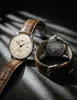 Two watches are displayed on a textured surface with dramatic lighting and shadows. Produktbild-Vorschau