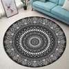 A round black and white mandala rug is placed on a light-colored floor next to a blue sofa and a framed picture of a deer. Produktbild-Vorschau