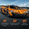 An orange toy car model with black accents, displayed on a dark gray road with a blurred background of a race track and sky. Anteprima dell’immagine prodotto